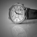 Elegant black and white close-up of a luxury wristwatch with a reflective stainless steel body and leather strap.